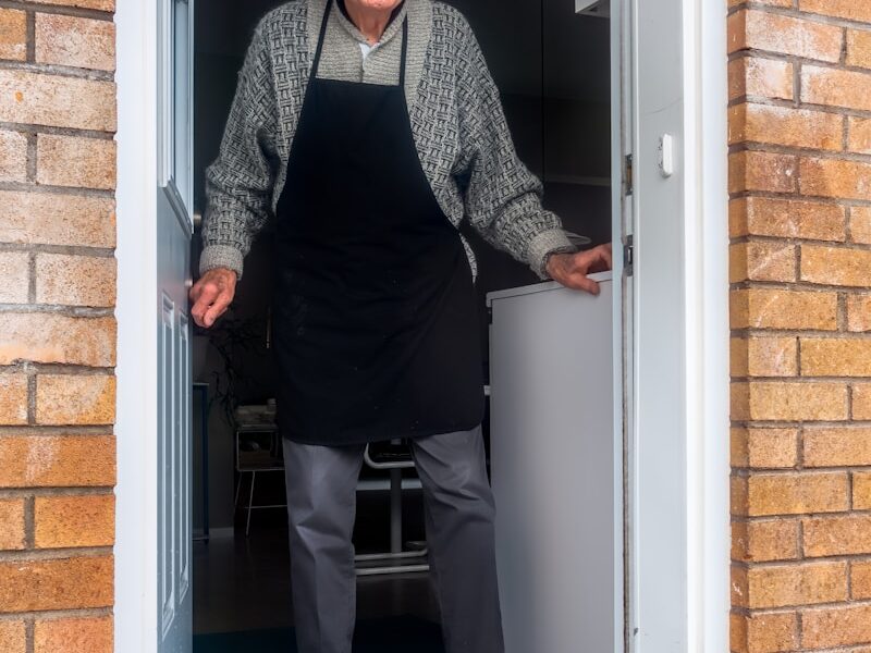 man in black vest and black dress pants standing beside white wooden door