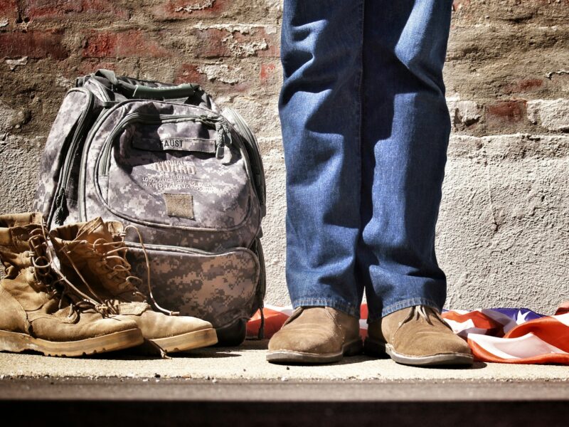 minimalist photography of person standing near backpack and boots